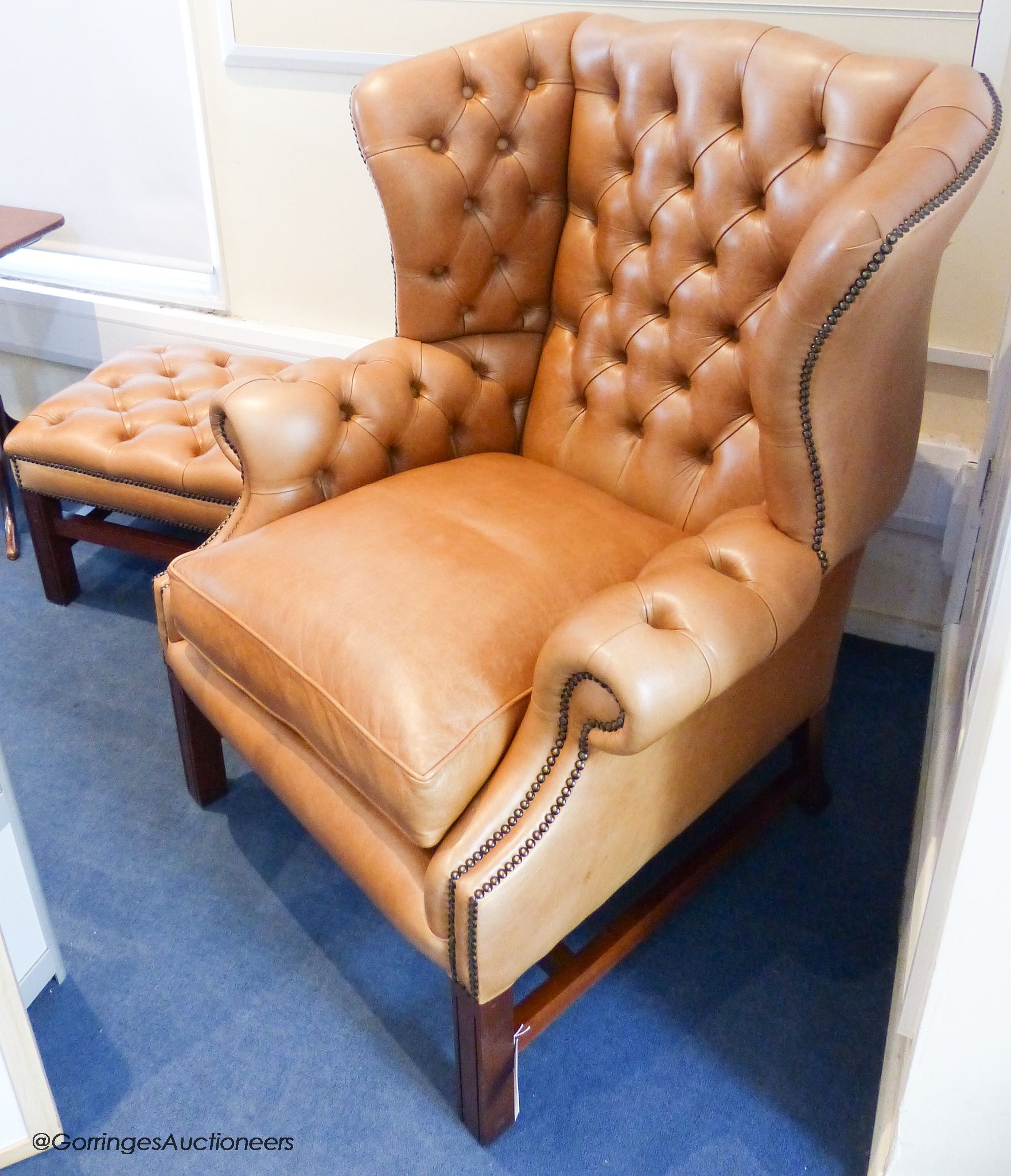 A pair of George III style buttoned tan leather wingback armchairs and two matching footstools